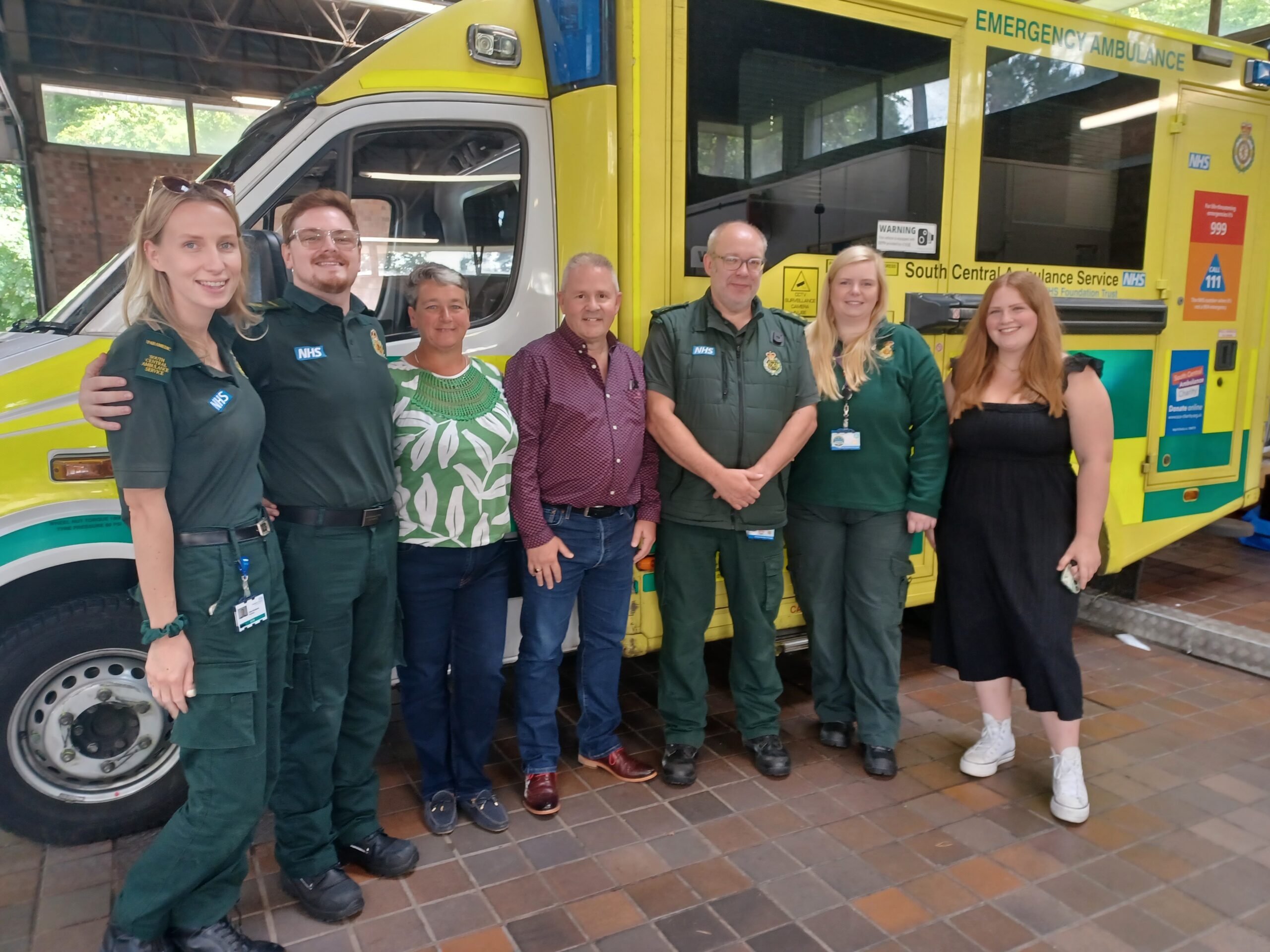 Two members of the public stand with ambulance staff in front of a vehicle