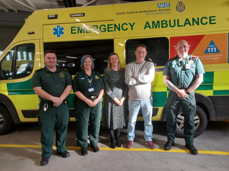 A man and woman standing with three ambulance service staff in front of an ambulance.