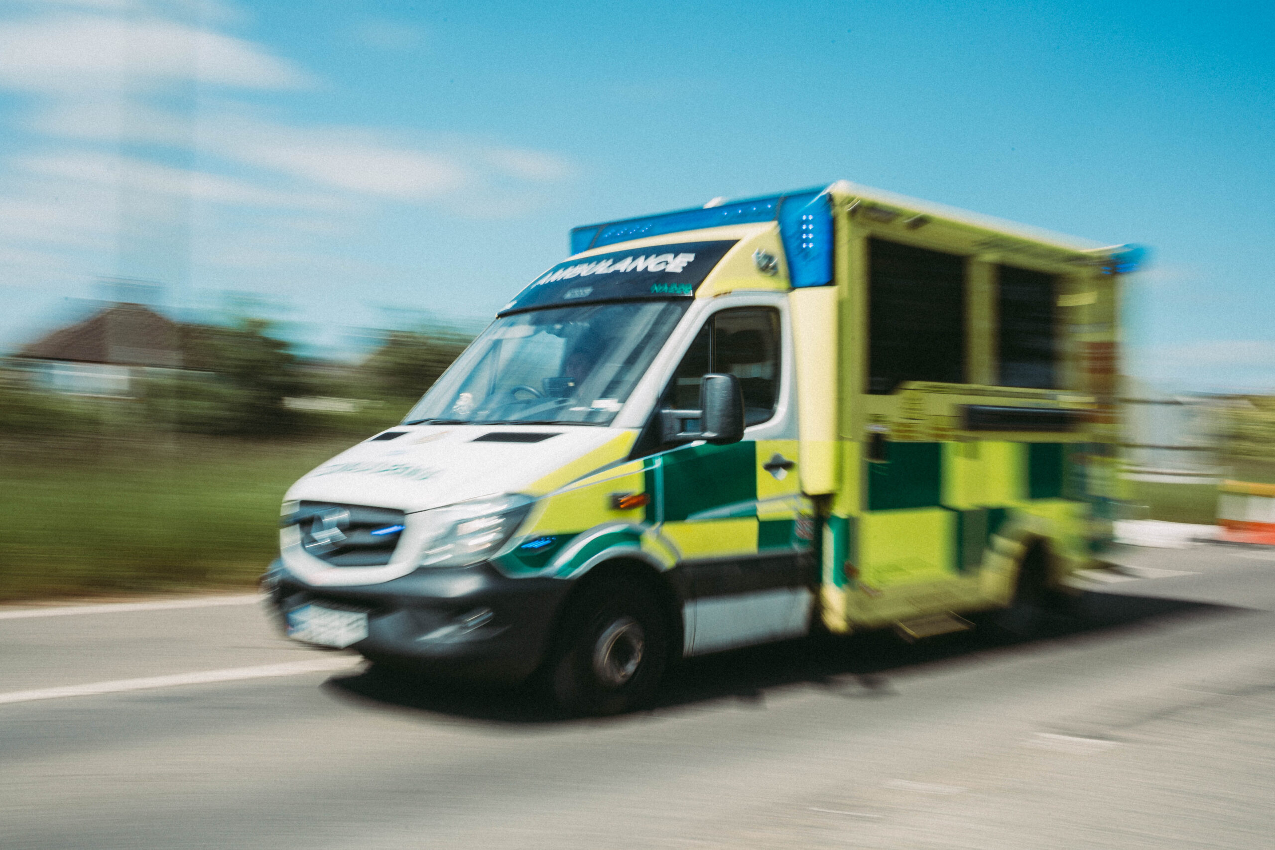 An ambulance on blue lights driving on a road. The image is slightly blurred to enhance the sense of speed it is travelling.