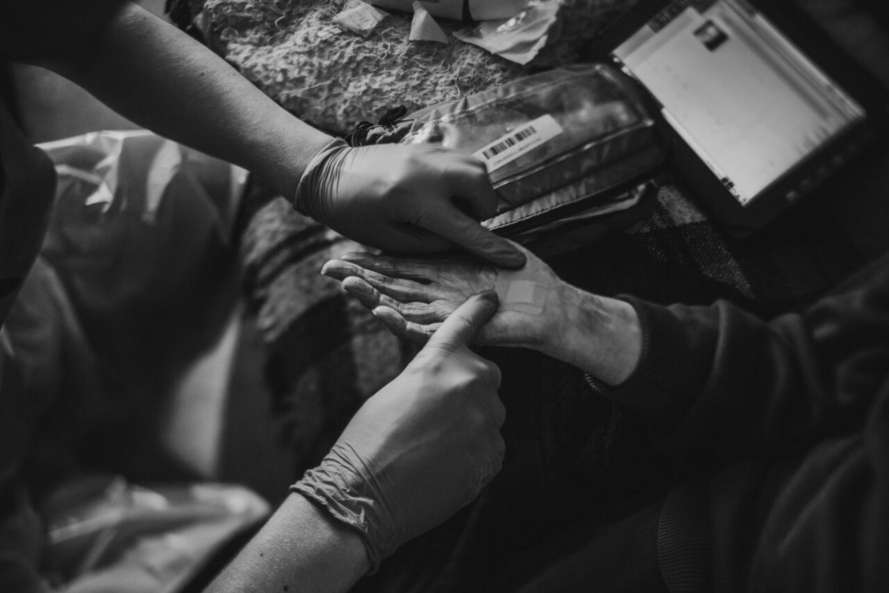 The gloved hands of a paramedic are taking observations from the hand of an elderly person