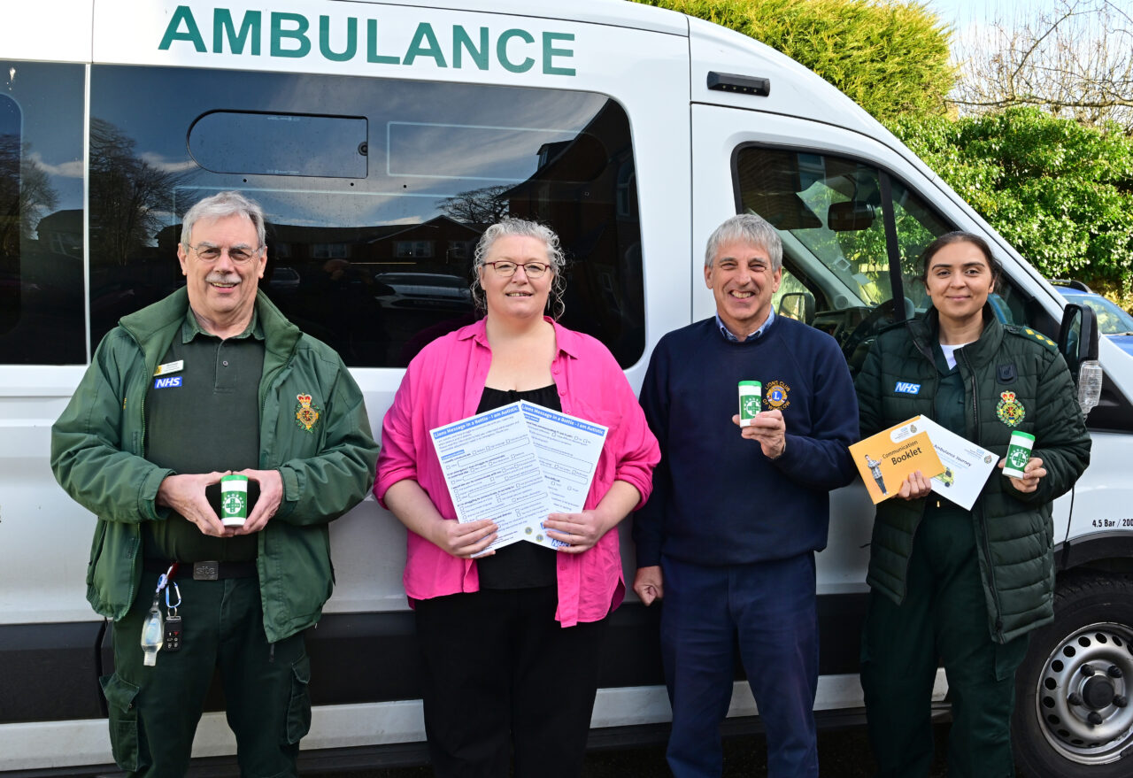 Four people standing in front of an ambulance with Message in a Bottle containers and new I Am Autistic forms